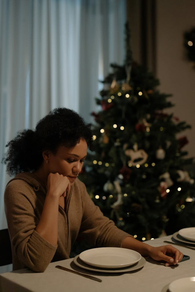 A solitary woman sitting at a dining table beside a decorated Christmas tree.